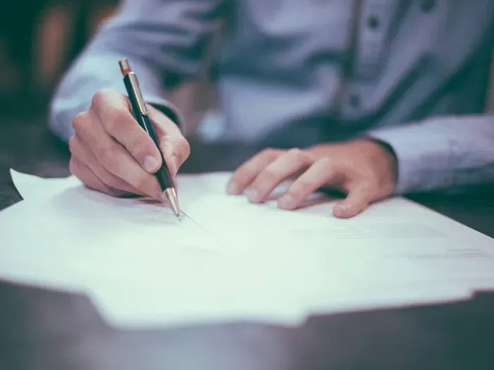Close view of hands signing forms with pen during an office meeting, showing trusted services on Local Bizzone Now